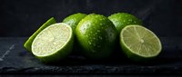 Fresh green limes whole and sliced on dark slate surface with water droplets for culinary cooking cocktails beverages kitchen food photography.