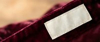 Burgundy velvet fabric with blank white label tag for branding and clothing manufacturing. Luxury textile material for fashion design and garment production.