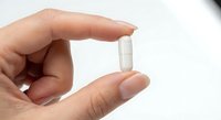 Hand holding white medical capsule pill between fingers on clean background for healthcare and pharmaceutical advertising.