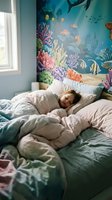 Young child sleeping peacefully in bed with colorful underwater ocean mural featuring coral reef, tropical fish and marine life on bedroom wall.
