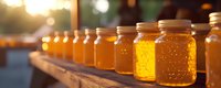 Golden honey in glass jars lined up on wooden surface with warm sunset lighting, suitable for food packaging, culinary blogs, organic product marketing, and agricultural business promotions.
