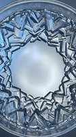 Shattered glass fragments arranged in circular pattern around white center space, creating abstract geometric composition with reflective surfaces and sharp edges.