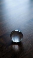 Clear crystal glass sphere resting on dark wooden surface with soft blue light, casting a delicate shadow in a moody, minimalist composition.