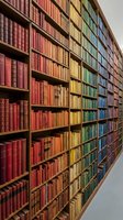 Library shelves filled with antique books arranged by color gradient from red through yellow, green, to blue, creating a rainbow effect. Wooden shelving unit displays vintage leather-bound volumes organized in rows. Suitable for education, literature, knowledge, and academic design projects.