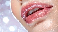 Sensual pink glossy lips with sparkly glitter makeup effect against soft bokeh background, close-up beauty shot for cosmetic and makeup advertising.