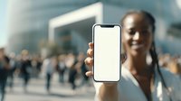 African American woman showing blank smartphone screen in busy urban environment with blurred crowd and modern buildings in background.