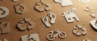 Eco-friendly cardboard cutout symbols on cork board, featuring recycling signs, footprint, house, bicycle, and green icons for sustainability concepts.