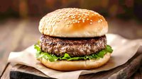 Juicy beef burger with sesame bun, fresh lettuce on rustic wooden board and craft paper. Close-up shot with selective focus for restaurant menu and food advertising.