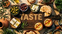 Rustic wooden board with the word TASTE surrounded by Mediterranean appetizers, olives, feta, hummus, and pita bread, top view flat lay.