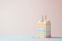 Pastel rainbow layered birthday cake slice with white frosting and lit candles on soft pink background, decorated with sprinkles and whipped cream swirls.