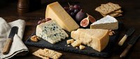 Gourmet cheese platter with blue cheese, brie, aged cheddar and crackers on dark slate board. Fresh figs, walnuts and wine pairing setup for entertaining.