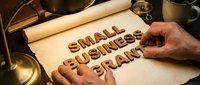 Small business owner hands arranging wooden letter blocks spelling small business start on parchment paper with vintage scale and magnifying glass.