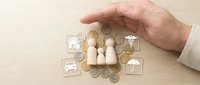 Hand protecting wooden family figures with insurance icons including home, car, health and umbrella symbols representing comprehensive coverage.