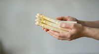 Fresh white asparagus spears held in hands against neutral background, suitable for food, cooking, healthy eating, and culinary design projects.