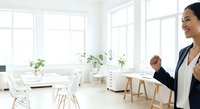 Young woman of East Asian descent, wearing professional business attire with navy blazer, presenting modern minimalist office space with natural light, potted plants, and contemporary furniture for corporate workspace design.