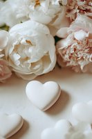 Delicate white heart decoration with soft pink and white peonies on light background, creating romantic wedding or Valentine's Day composition.
