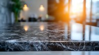 Dark marble countertop with natural veining pattern in luxury kitchen interior, soft bokeh lights and sunflare through window create warm atmosphere.