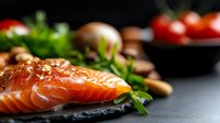 Fresh raw salmon fillet on black stone plate with herbs, garlic and spices. Close-up with selective focus on pink fish meat texture for culinary background.