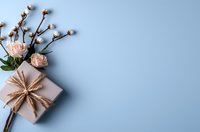 Minimalist flat lay composition with craft paper gift box, twine bow, delicate pink roses and cotton branches on soft blue background with copy space.