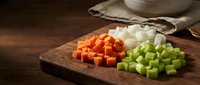 Fresh diced carrots and celery on wooden cutting board for healthy cooking and meal preparation in rustic kitchen setting.