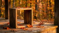 Wooden frame structure sitting on forest ground surrounded by fallen autumn leaves with blurred golden foliage background, suitable for seasonal marketing and fall-themed design projects.