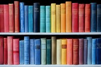 Colorful vintage hardcover books arranged on wooden shelves, spines showing rainbow spectrum from red through blue, creating organized library collection display.