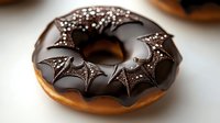 Chocolate glazed donut decorated with dark bat wings pattern made with chocolate sprinkles on brown background, Halloween themed dessert treat.