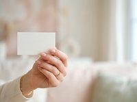 Hand holding blank white business card or note in modern interior space with soft blurred background, suitable for branding and corporate design projects.