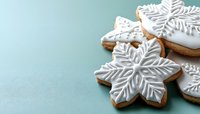 Festive snowflake sugar cookies decorated with white royal icing on light blue background. Winter holiday baking and traditional Christmas treats.