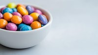 Colorful candy coated chocolate balls in white ceramic bowl on light background. Sweet treats in vibrant orange, pink and blue colors for dessert or snacking.