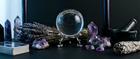 Mystical crystal ball with amethyst gems, sage bundle and healing stones arranged for spiritual divination and meditation practice on dark surface.
