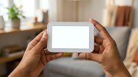 Person with dark skin tone holding white tablet device with blank screen in modern home interior setting for app mockup and digital content display.