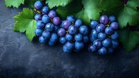 Fresh ripe dark blue grapes with green leaves on black stone background, macro view of juicy berries with natural lighting and moody atmosphere.