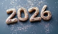 Chocolate cookies shaped as numbers 2026 sprinkled with powdered sugar on dark background. Festive holiday baking concept for New Year celebration.
