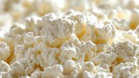 Fresh cottage cheese macro shot showing soft white curds and creamy texture with natural light highlighting delicate dairy details. For food photography and packaging.