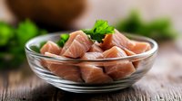 Fresh raw salmon cubes in glass bowl with parsley garnish on wooden table for cooking and meal preparation.