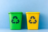 Green and yellow recycling bins with black recycle symbol against blue wall background, minimalist eco-friendly waste sorting concept for sustainable living.