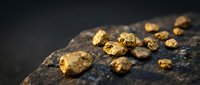 Raw gold nuggets scattered on dark rock surface showcasing natural precious metal mining discovery and wealth investment opportunities.