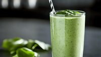 Fresh green smoothie with spinach leaves garnish in tall glass on dark background, healthy breakfast drink with straw and natural ingredients.