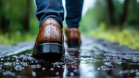 Brown leather brogue shoes walking on wet pavement with water splashes and reflections, close-up view against blurred green nature background.