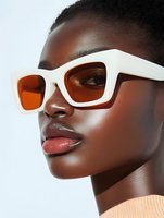 Young African woman wearing trendy white rectangular sunglasses with orange lenses, close-up portrait showing glossy lips and flawless dark skin against light background.