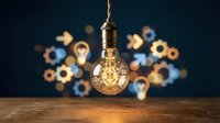 Glowing vintage Edison bulb hanging on rope cord with blurred lightbulbs and gears in background. Creative innovation and brainstorming concept for business.