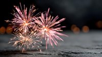 Vibrant pink and gold fireworks exploding against dark night sky, creating festive atmosphere for celebration events.