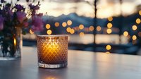 Glowing candle in crystal glass holder on table with bokeh lights and sunset background creates cozy romantic atmosphere for evening relaxation or celebration.