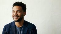 Happy young African American businessman in navy suit smiling confidently against neutral background for corporate marketing and professional headshot use.
