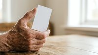 Senior man holding blank white card on wooden table with window background for business messaging.