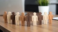 Diverse wooden human figures standing together on office desk representing teamwork, inclusion, unity and corporate diversity in modern workplace.