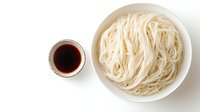 Fresh white rice noodles in ceramic bowl and soy sauce in small dish on white background, overhead view of traditional Asian ingredients for cooking.