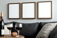 Three empty wooden frames on gray wall above dark sofa, with wine glasses and bottle on side table creating modern living room gallery wall mockup.
