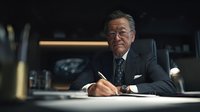 Senior Caucasian businessman in elegant suit writing at executive desk in modern office with dramatic lighting for corporate and professional concepts.